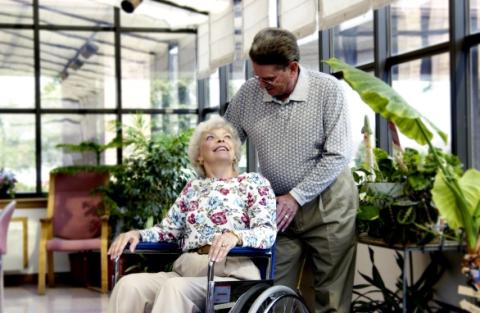 A man assists an elderly woman in a wheelchair.