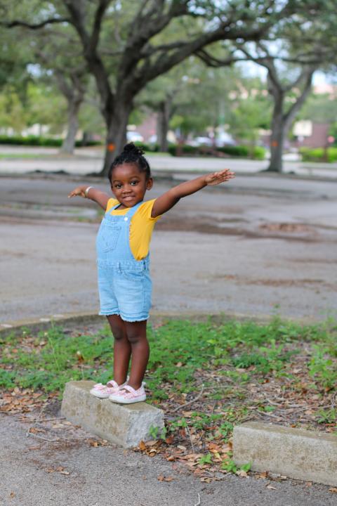 Child wearing yellow shirt, standing on concrete block with arms outstretched on both sides